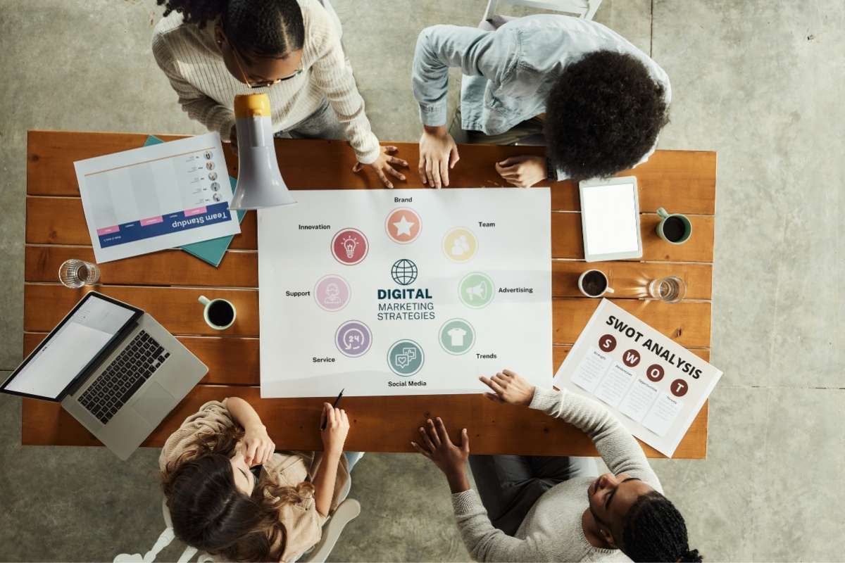 Des personnes autour d'une table discutent des stratégies de marketing digital, avec des documents et un ordinateur portable visibles.